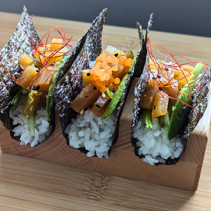Two hand rolls (temaki): one shaped like a traditional cone with nori wrapped around rice and fillings, and the other served open-faced in a taco-style presentation. Both are plant-based and displayed side by side.