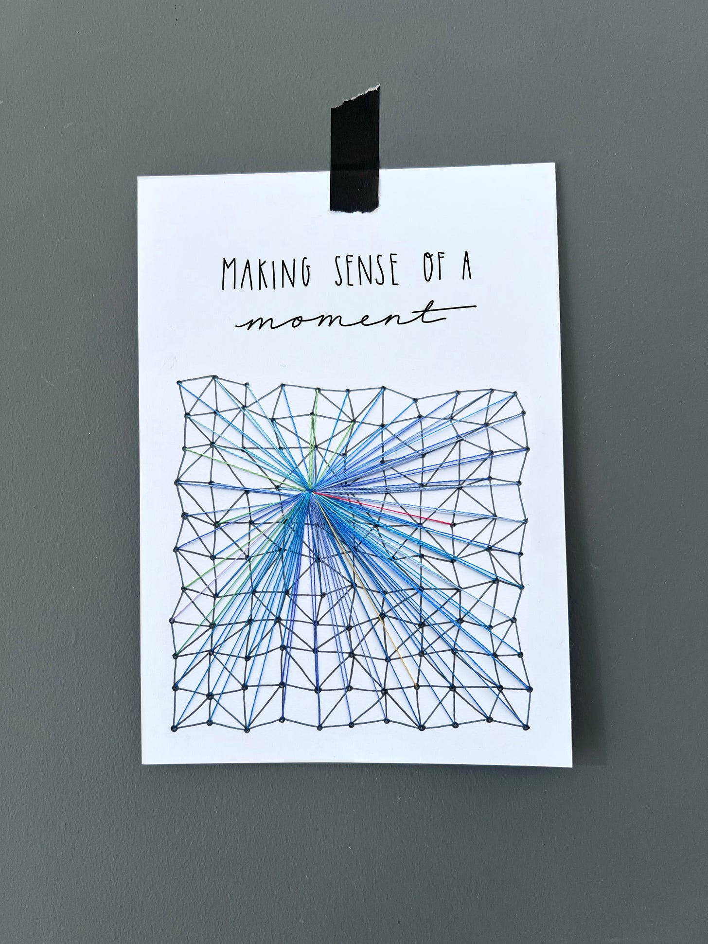 Embroidered artwork on paper with the title “Making sense of a moment.” A black geometric grid contains 100 coloured threads radiating toward a single central point. Most threads are blue (vision), with a few green (touch), red (sound), yellow (smell), and lilac (balance). The design symbolises sensory input converging into conscious awareness.
