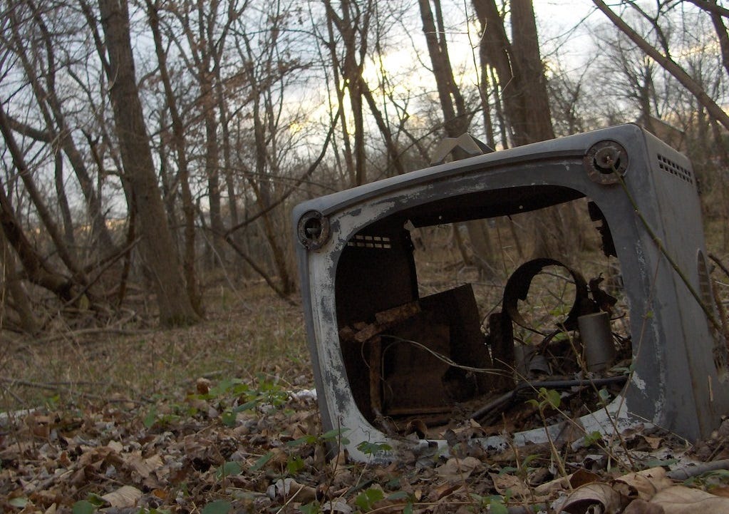 photo, in very muted colors, of a screenless old TV that's been sitting in some woods for years. Fallen leaves from the bare trees are all over he ground, and the rusty innards of the TV can be seen inside the weathered metal frame. To add to the surreal quality of the image, the photo was taken slightly angled to the left. photo, in very muted colors, of a screenless old TV that's been sitting in some woods for years. Fallen leaves from the bare trees are all over he ground, and the rusty innards of the TV can be seen inside the weathered metal frame. To add to the surreal quality of the image, the photo was taken slightly angled to the left.