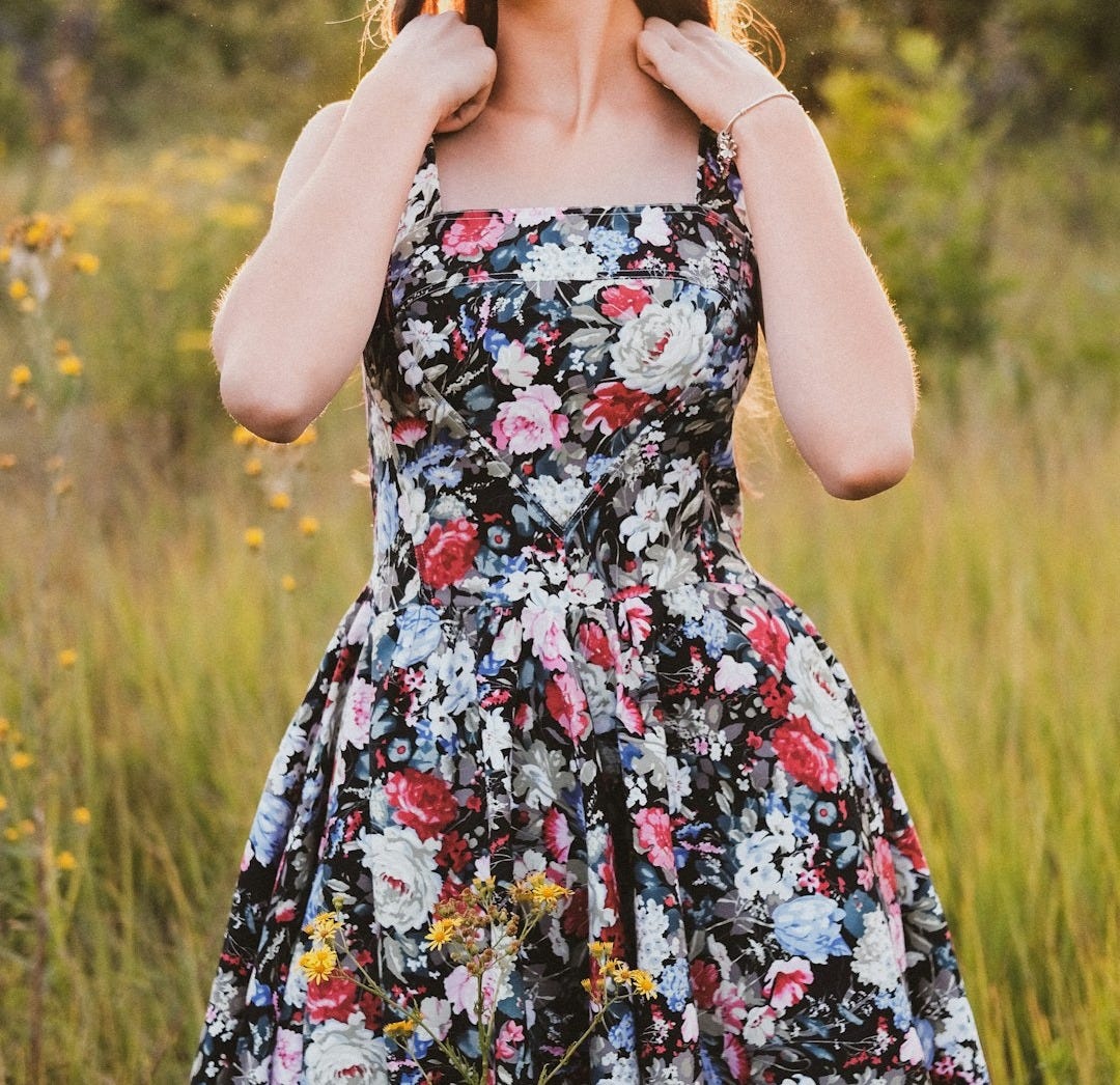 woman in black red and white floral spaghetti strap dress standing on green grass field during woman in black red and white floral spaghetti strap dress standing on green grass field during
