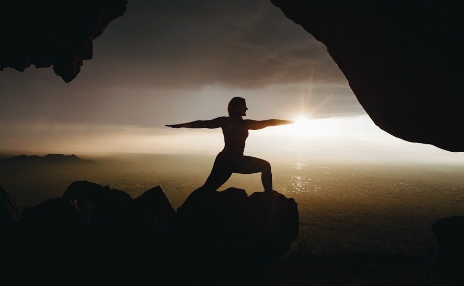 silhouette of person in yoga post on top of cliff during sunset