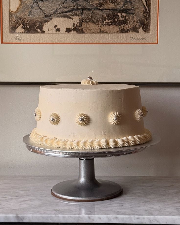 This may contain: a white cake sitting on top of a metal stand in front of a framed painting