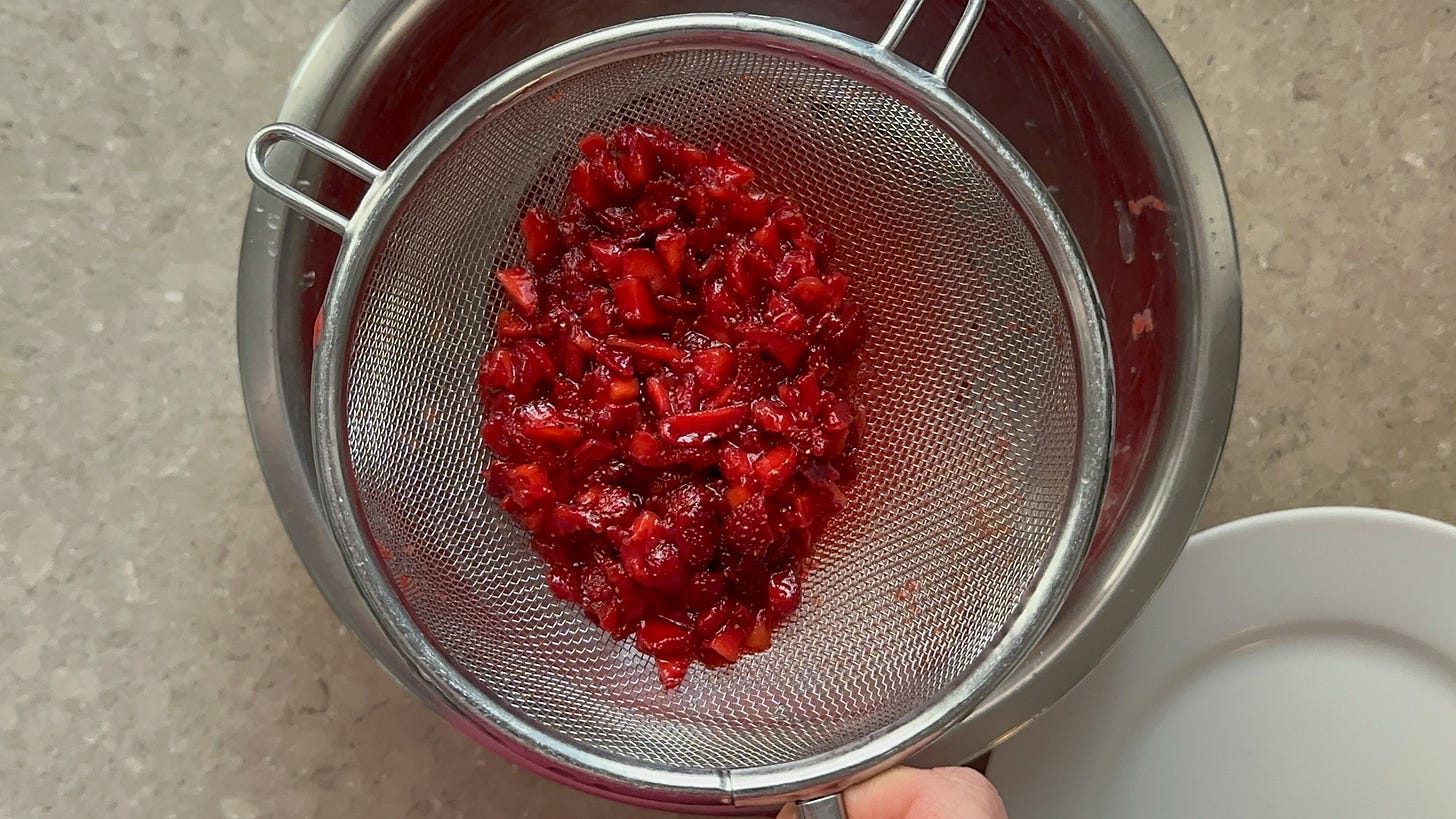 A photo of macerated bits of strawberry in a metal strainer.
