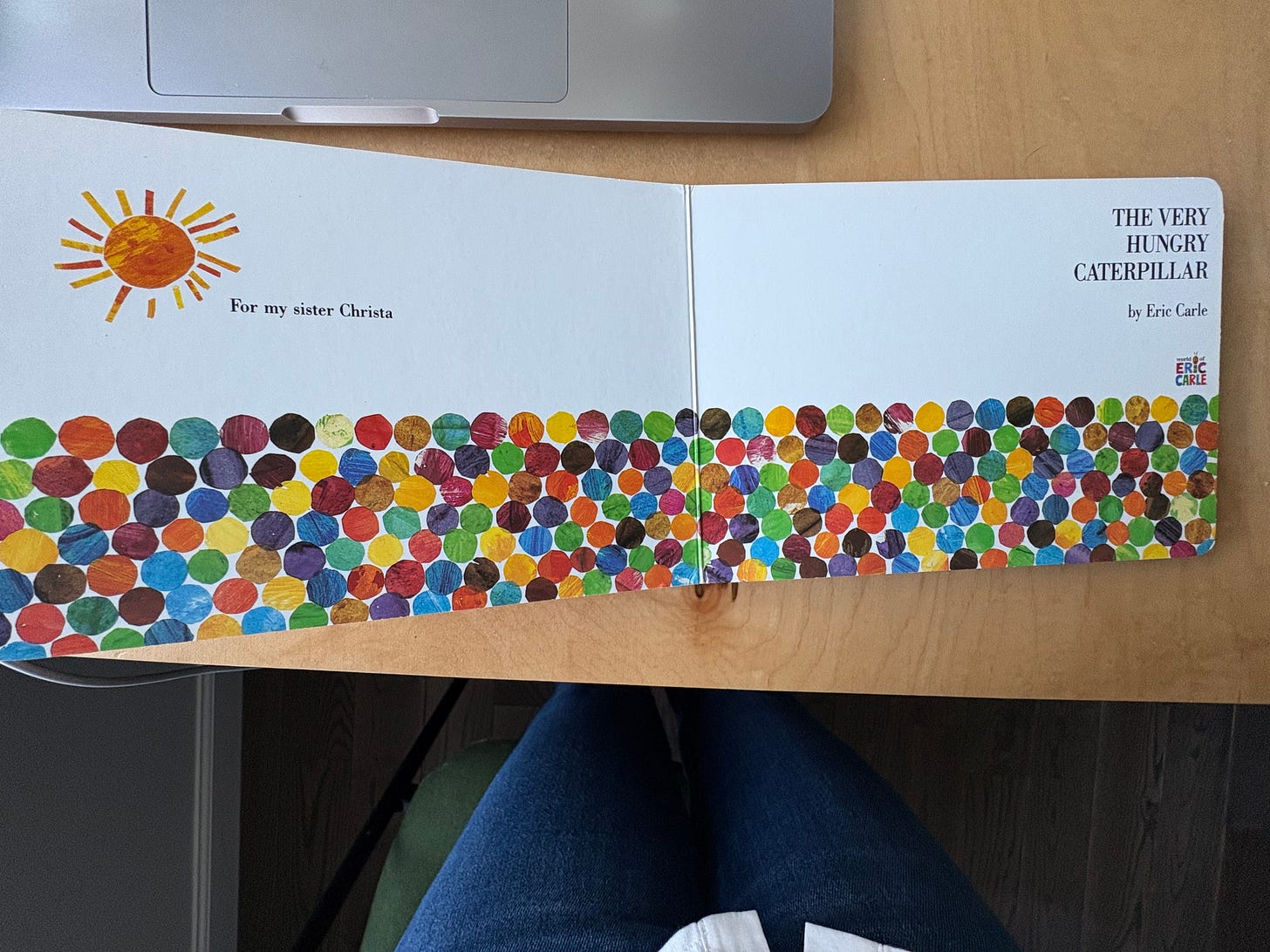 Title and dedication page of the book the Very Hungry Caterpillar. title and dedication page of Title page of The Very Hungry Caterpillar. On the left side there is an illustrated orange sun and the words “For my sister Christa”. On the right side the title and author are reprinted. Across the bottom of both pages is an array of different-colored illustrated dots.