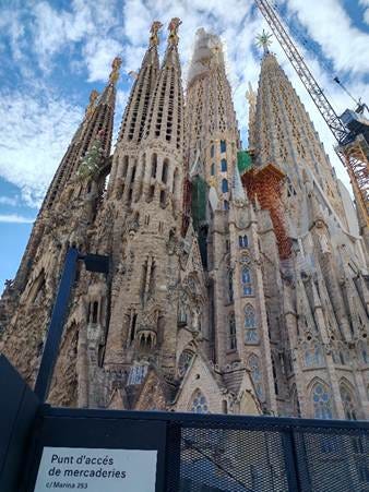 Un edificio alto con muchas torres con la Sagrada Familia al fondo. El contenido generado por IA puede ser incorrecto.