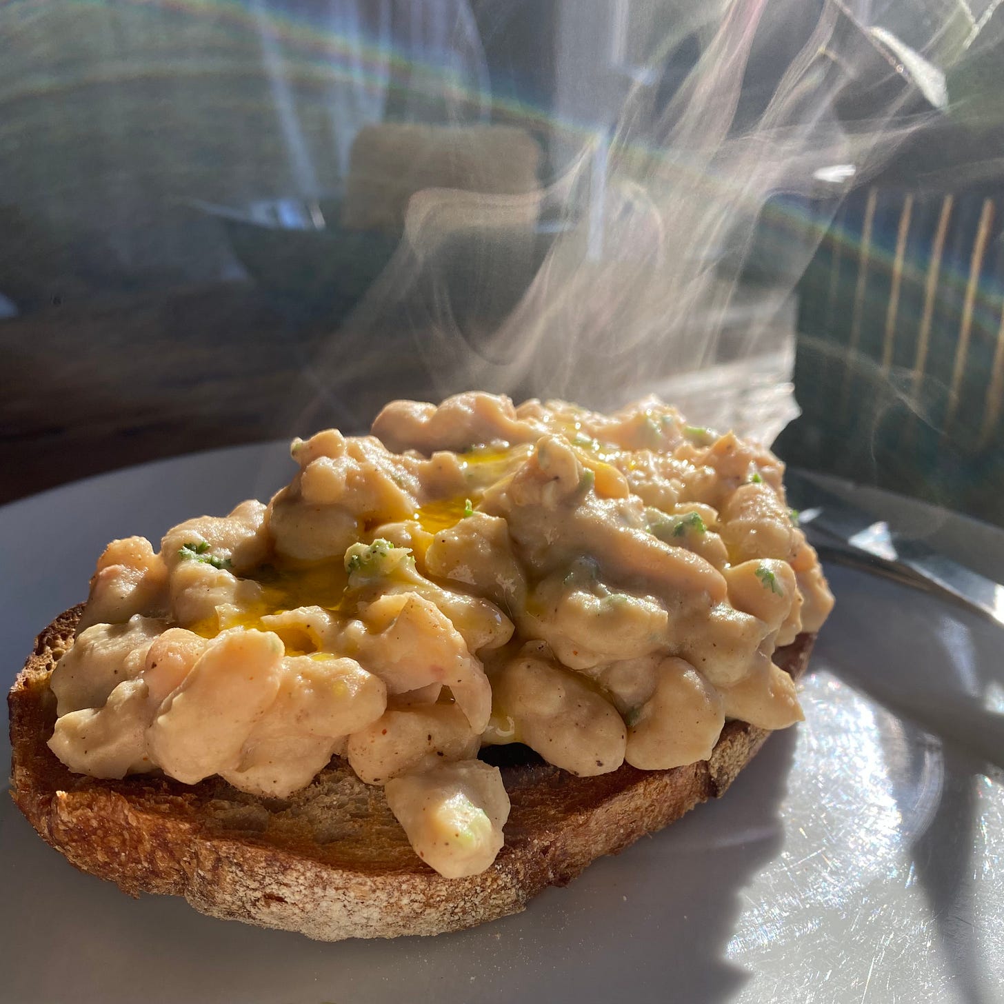 White plate topped with a piece of sourdough toast covered in hot cannellini beans, with fresh parsley
