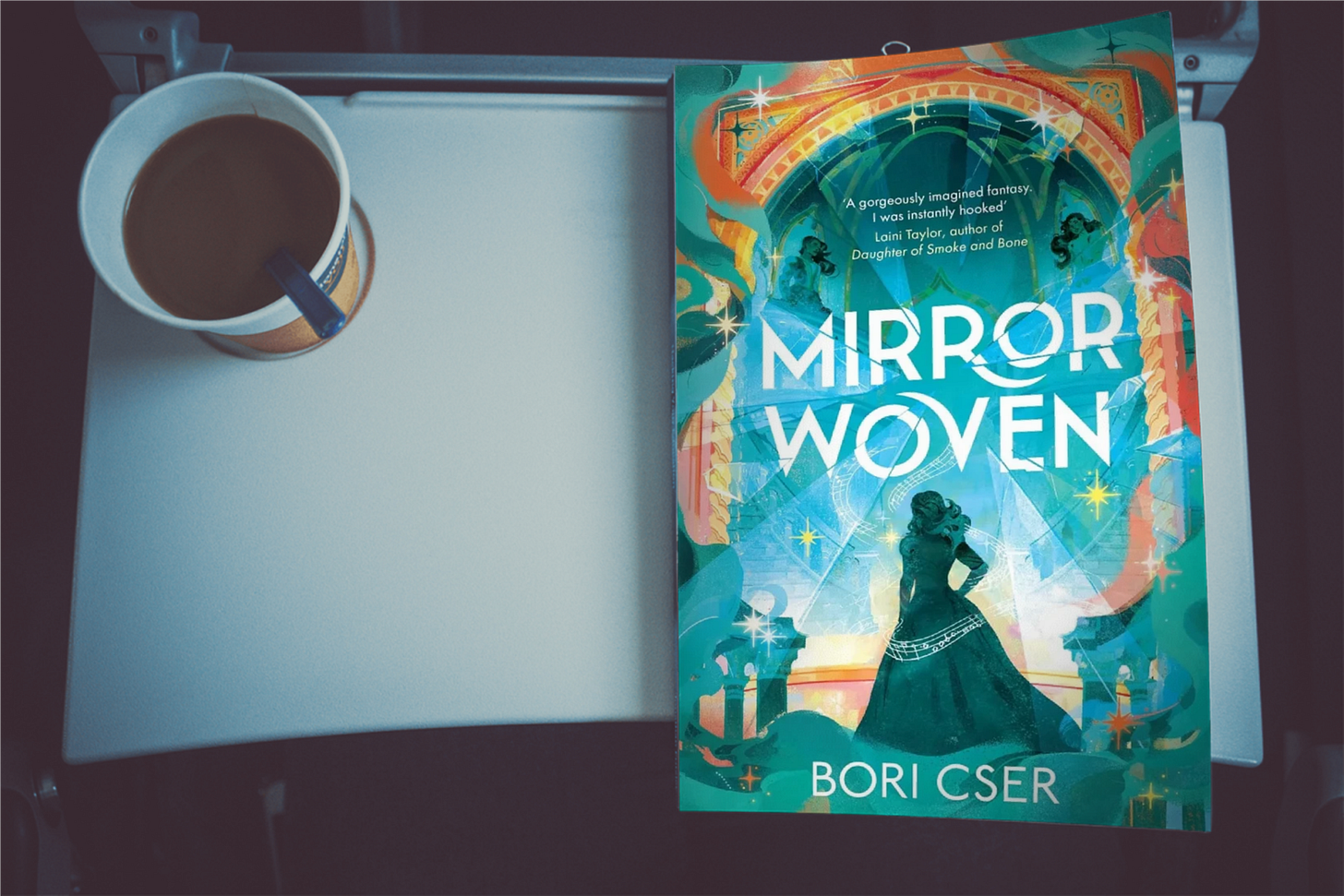 Book "MirrorWoven" by Bori Cser on a table next to cup of coffee Book "MirrorWoven" by Bori Cser on a table next to cup of coffee