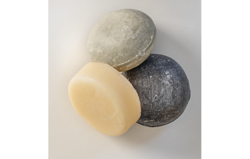 Two round bars of shampoo with a disk of conditioner leaning against them.