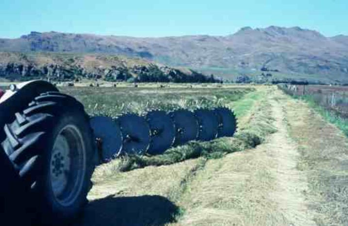 A long tedder with round metal wheels covered in tines turns the dried hay over to expose the damp grass underneath. A long tedder with round metal wheels covered in tines turns the dried hay over to expose the damp grass underneath.