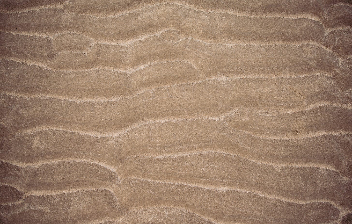 a birds eye view of beach sand shortly after the tide goes out, thus invoking a feeling of the hard grooves of the sand left by the waves. 