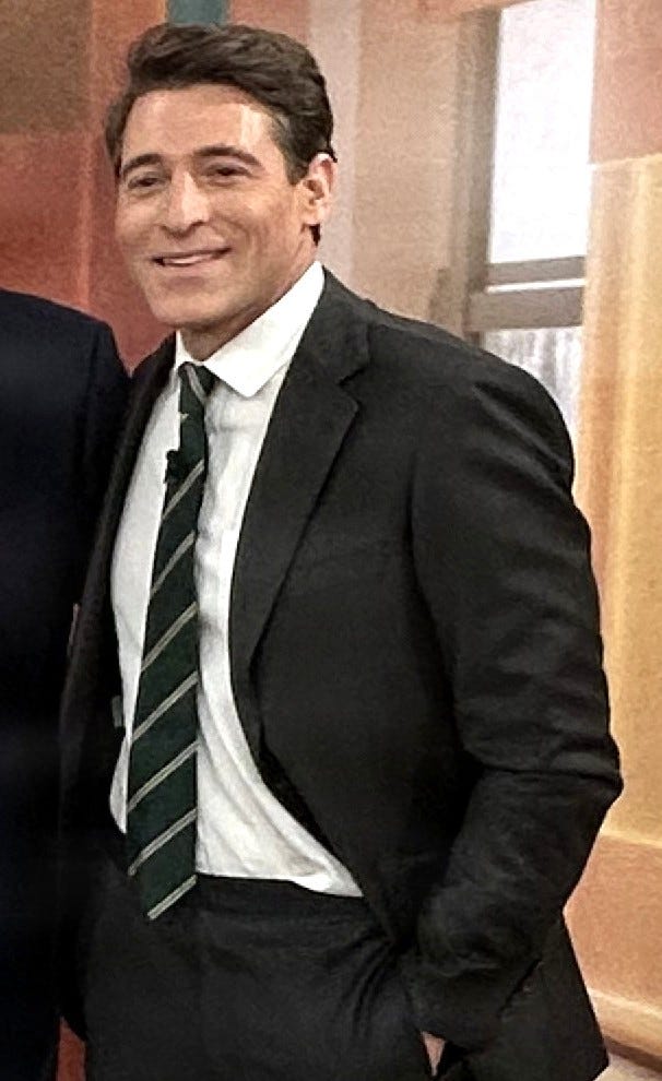 White guy with brown hair in dark suit and tie, standing in panelled room; left hand in pocket, someone stnading to his right, mostly cropped out White guy with brown hair in dark suit and tie, standing in panelled room; left hand in pocket, someone stnading to his right, mostly cropped out