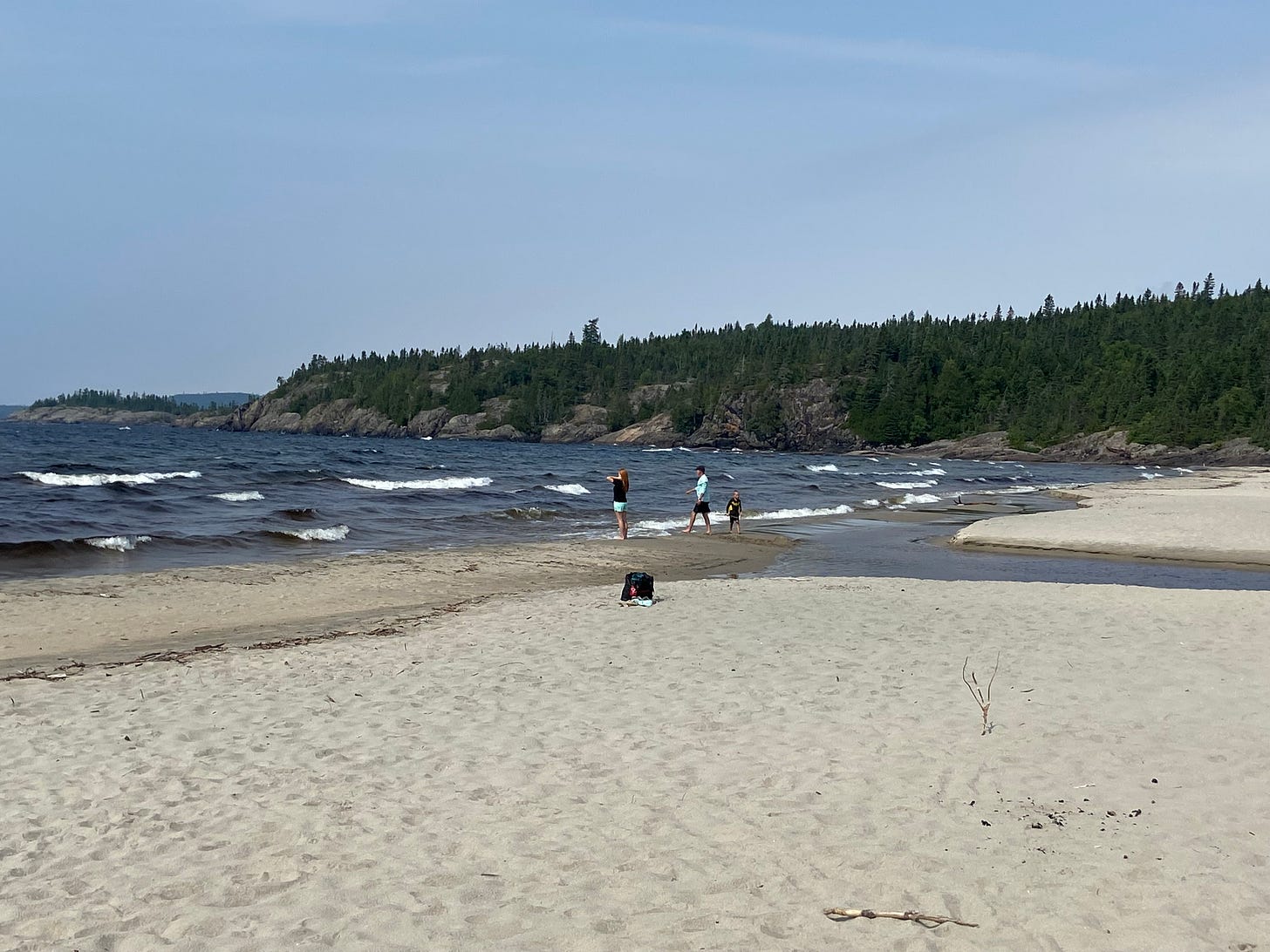 Pic of a sandy beach on Lake Superior, with cliffs and trees in the background