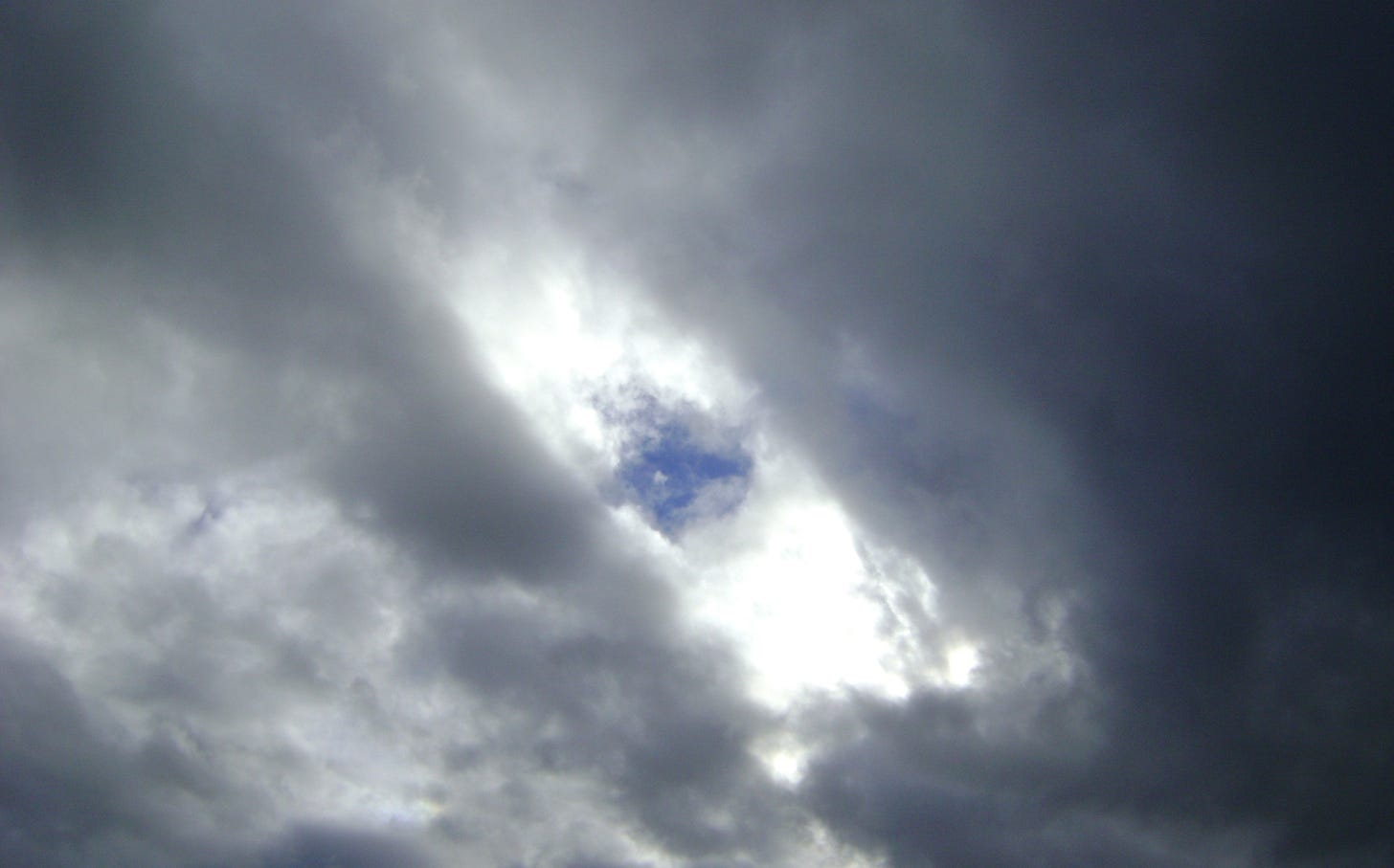 Image is of a dark sky with a patch of blue peeking through the clouds. Image is of a dark sky with a patch of blue peeking through the clouds.