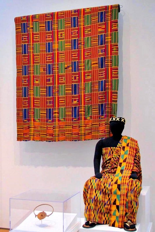A colorful robe is worn by a seated dummy while a similarly colorful tapestry hangs on the wall behind it. A colorful robe is worn by a seated dummy while a similarly colorful tapestry hangs on the wall behind it.