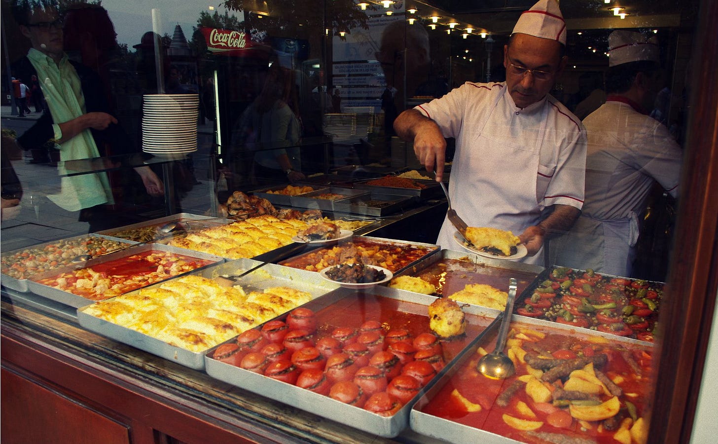 Interior of a Turkish lokanta with trays of food displayed behind a counter and diners sharing meals