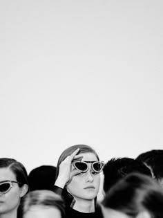 This may contain: a black and white photo of a woman with sunglasses on her head in front of a group of people