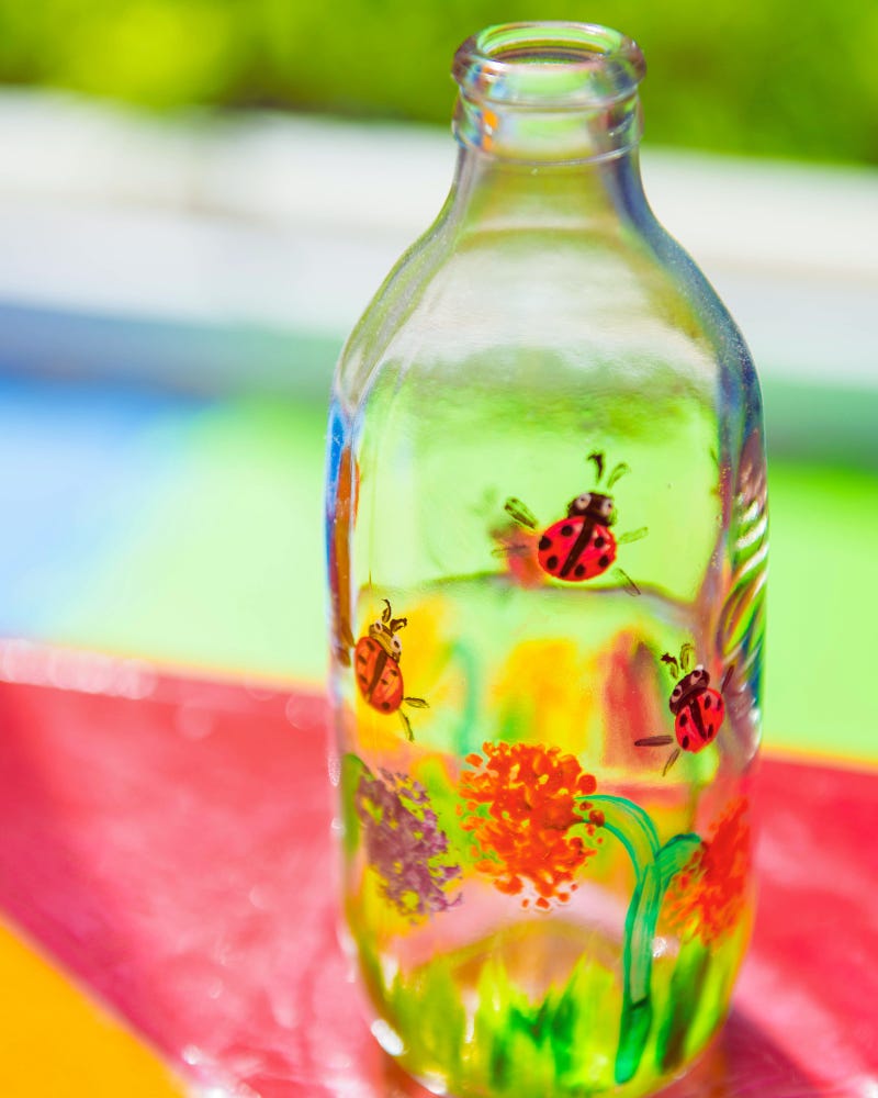 A clear glass bottle painted with small red ladybugs after someone learned how to paint glasses with acrylics A clear glass bottle painted with small red ladybugs after someone learned how to paint glasses with acrylics