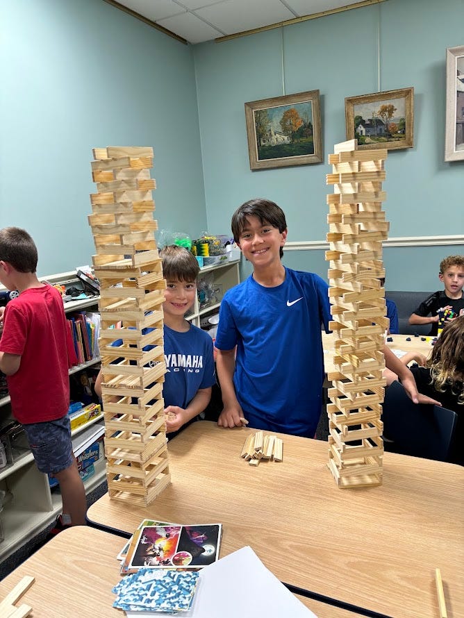 Two kids smiling with their keva plank towers which are taller than they are.