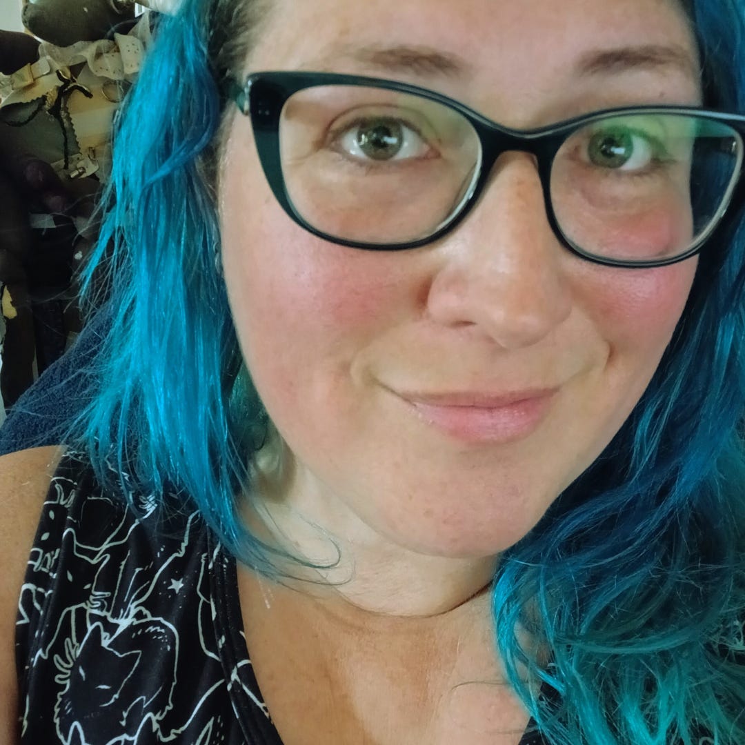 image of a smiling woman with blue hair and glasses