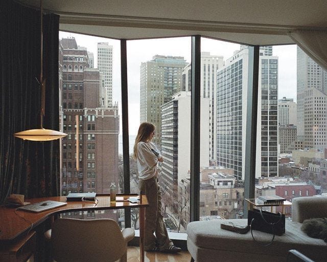 This may contain: a woman standing in front of a window looking out at the cityscape and skyscrapers