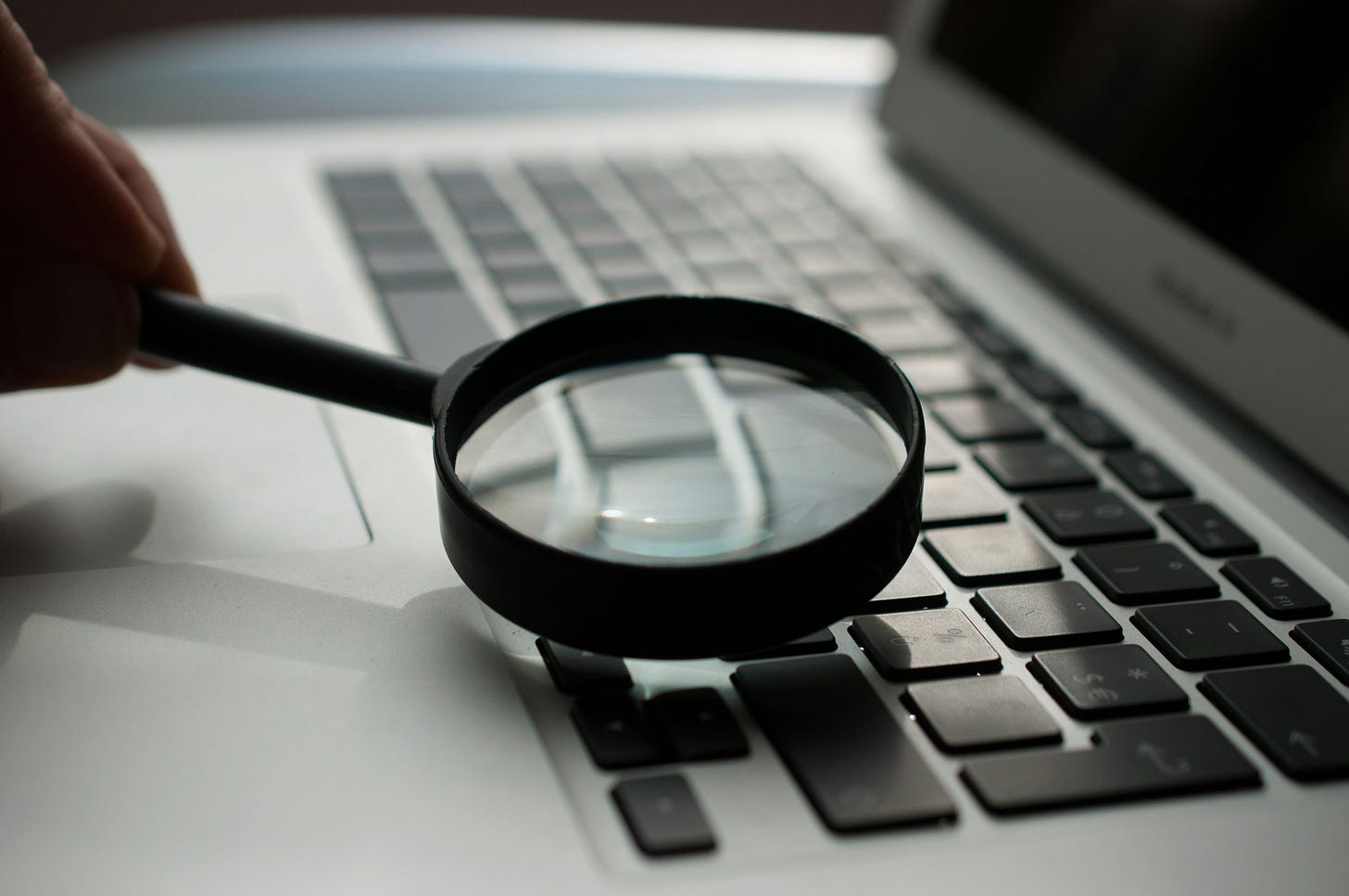 A magnifying glass seen side on, held over a laptop keyboard