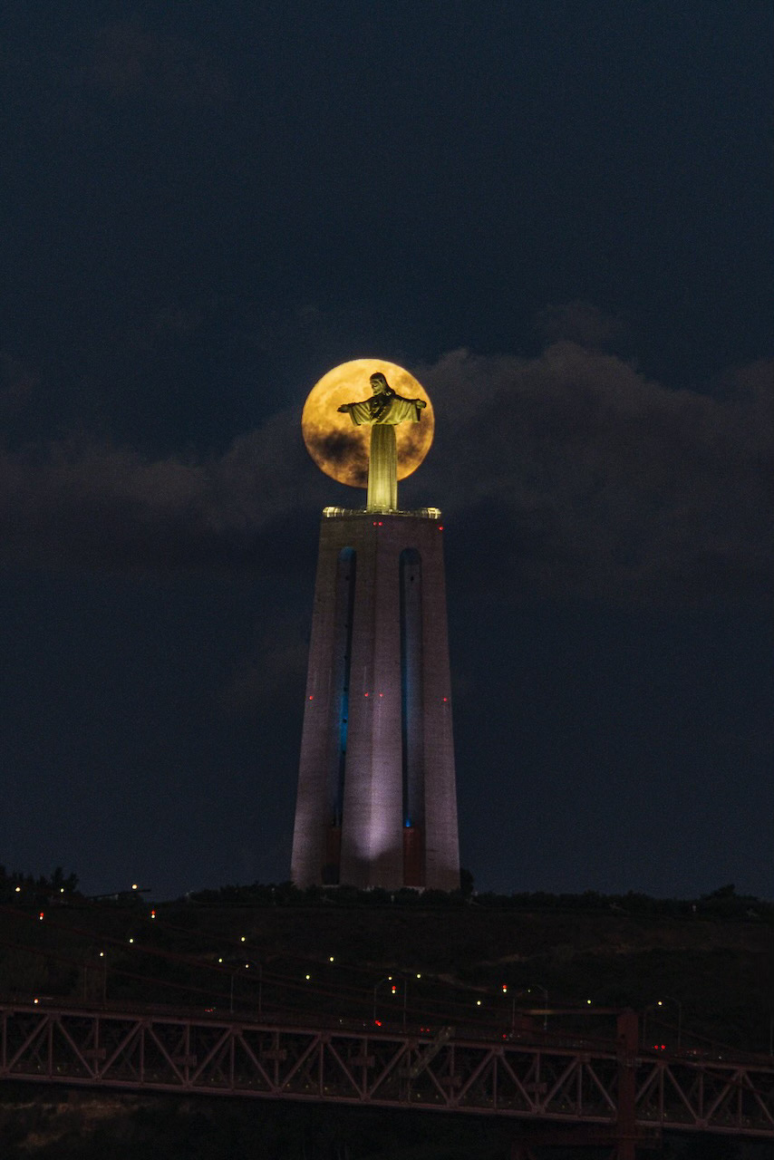 The full moon frames and illuminates the statue of Cristo Rei in Lisbon.