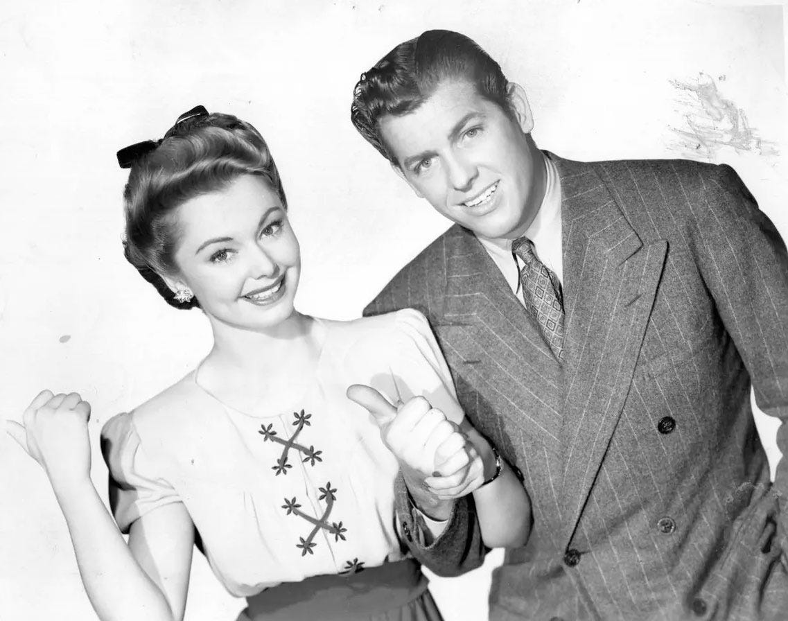 Jean Heather and James Brown in a publicity still from 1944 film Going My Way. They lift their thumbs as if to hitchhike and smile happily