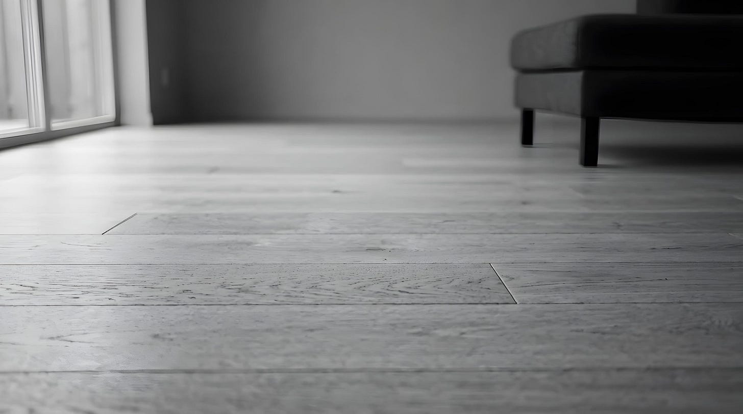An oak plank floor seen from low to the ground, with the base of an ottoman and a window beyond.