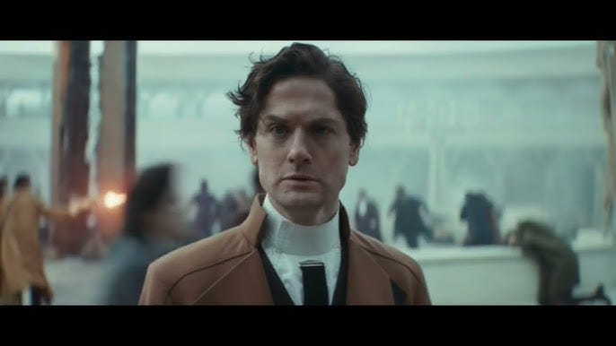 image of the character Syril Karn from the TV show Andor. He is standing in a plaza, looking bewildered, as a fight between fascists and rebels erupts all around him