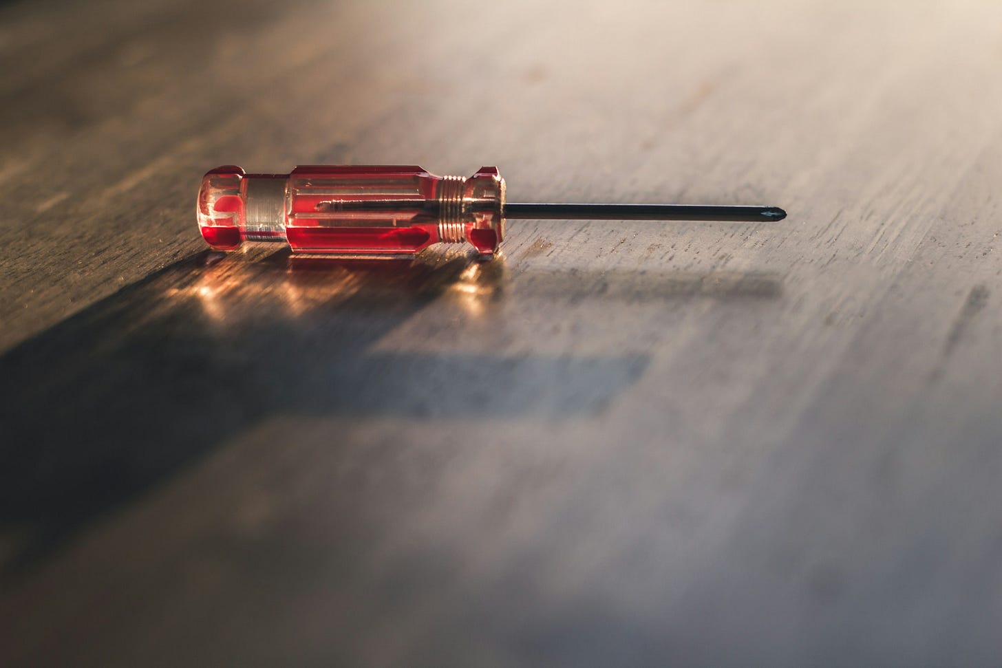 Ripresa ravvicinata di un cacciavite con il manico rosso e un po' smerigliato, appoggiato su un tavolo di legno su cui arriva dal fondo una luce tenue. Ripresa ravvicinata di un cacciavite con il manico rosso e un po' smerigliato, appoggiato su un tavolo di legno su cui arriva dal fondo una luce tenue.