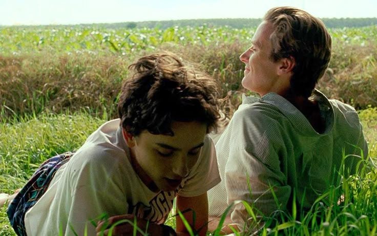 This may contain: two people sitting in the grass looking at each other