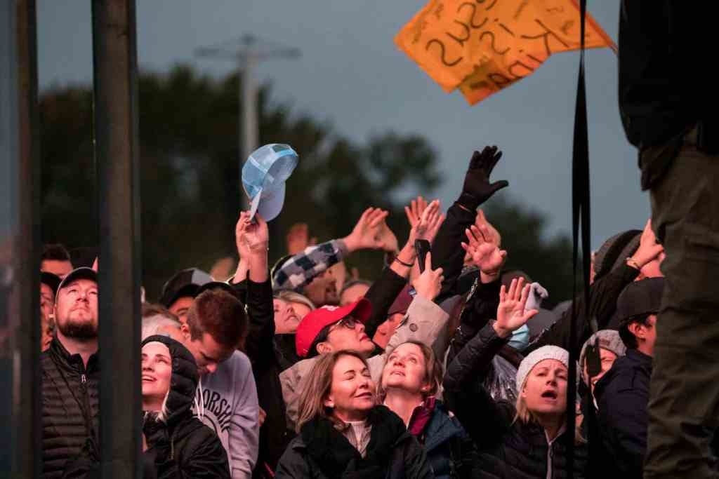Crowd of people in winter clothes stand with their hands and faces raised in worship