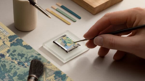 A close-up of a hand holding a precision painting instrument above a miniature painting on a postage-stamp-size metal plate.