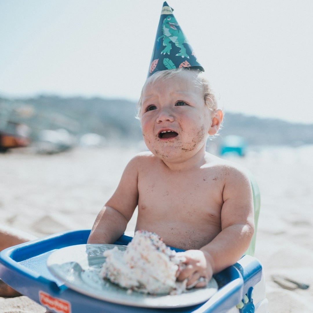 topless baby sitting on blue plastic bath tub on beach during daytime