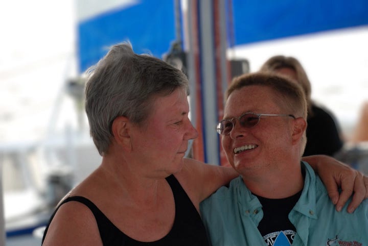 A large golden seated Buddha statue at Dambulla, Sri Lanka, surrounded by dense green forest and temple buildings. – A photo of two people smiling at each other in an affectionate moment aboard a boat, one with short grey hair and a black tank top, the other with short-cropped hair, glasses, and a turquoise shirt. – A historic half-timbered town hall building with three pointed towers, located in Einbeck, Germany. – A wide landscape view of the town of Einbeck seen from above, with green trees in the foreground and rolling hills under a partly cloudy sky. – A photo of a red house with white trim and steep tiled rooflines, surrounded by green hedges and bushes. – A portrait of a person with short-cropped hair wearing a blue and white rugby-style shirt, shown against a transparent background. – A color photograph of Monument Valley showing red sandstone formations under a blue sky. – A stylized digital artwork of Table Mountain in bright red, set against a textured blue background with abstract shapes and color overlays.