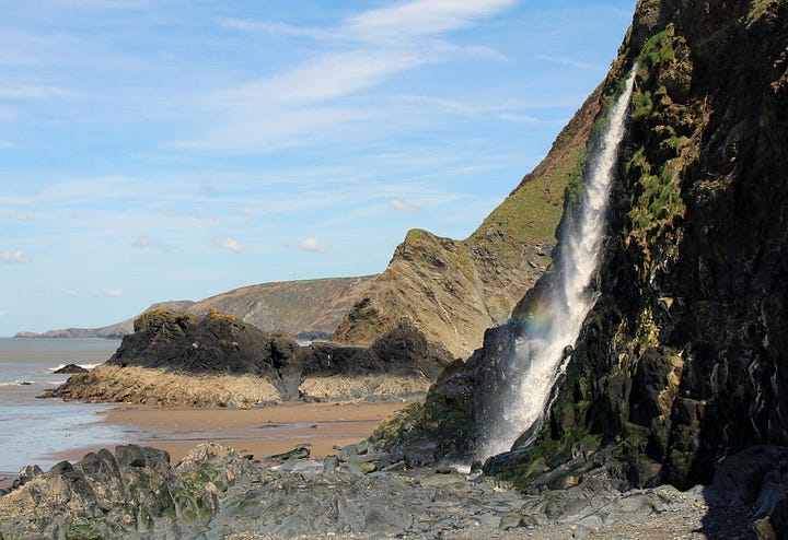Two side-by-side images of Tresaith in Wales. The left image shows the sandy beach, jagged cliffs, and the coastal village nestled in the green hillside. The right image shows a waterfall cascading down a dark, steep rock face directly onto the sandy beach below.