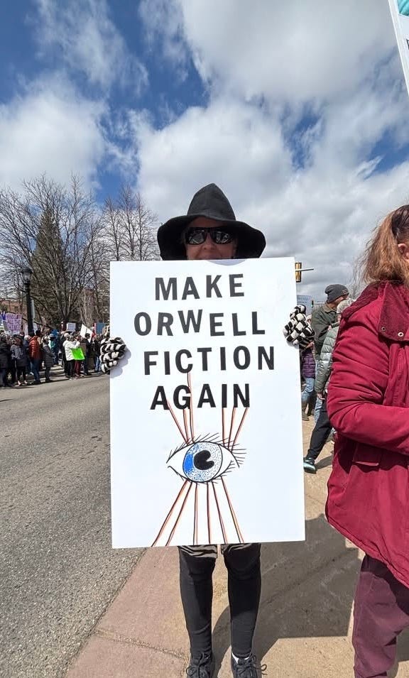 woman holding a sign reading make Orwell fiction again