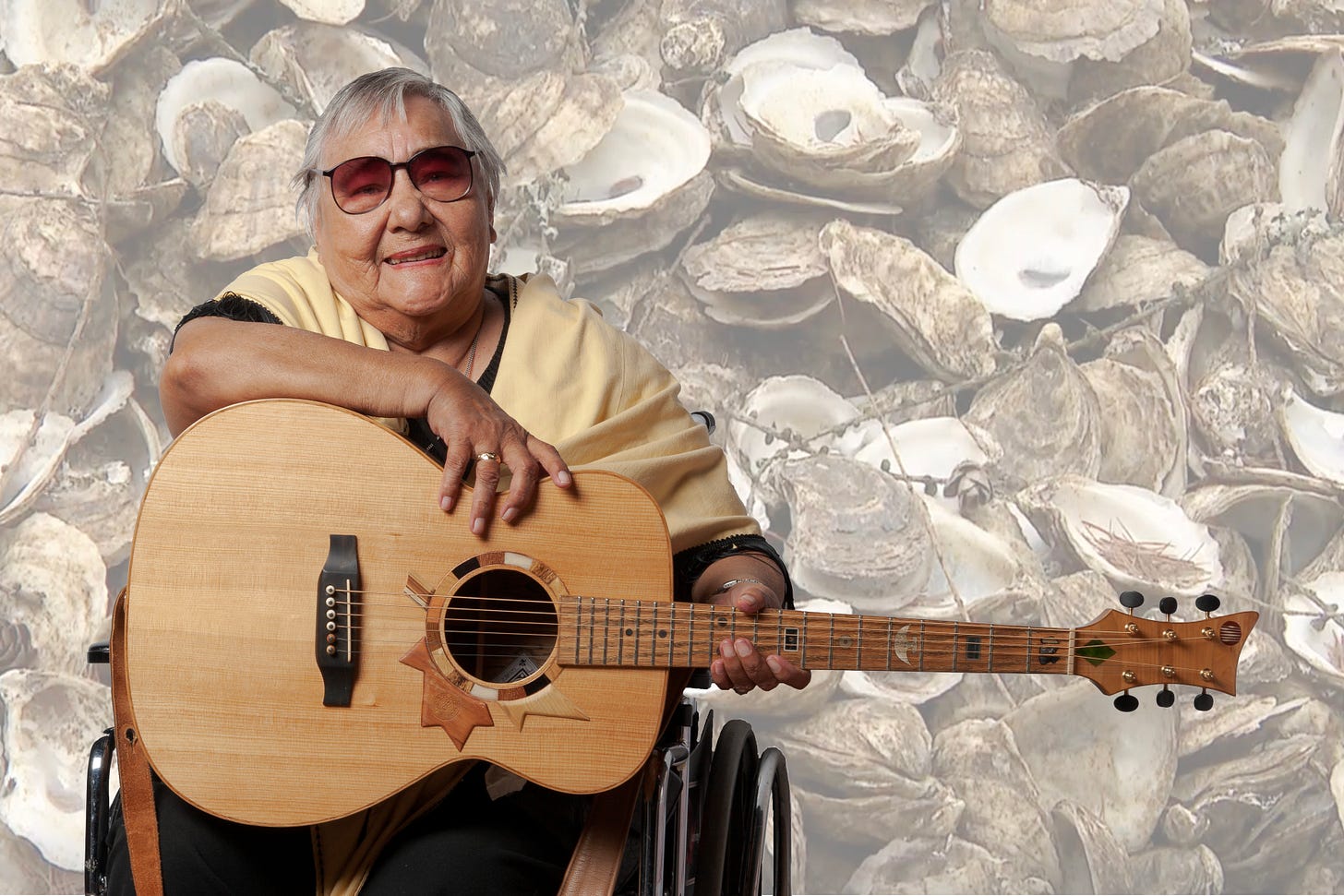 Portrait of Genevieve Labobe-Phillips in a wheelchair holding Voyageur laid over an image of a pile of dead oysters Portrait of Genevieve Labobe-Phillips in a wheelchair holding Voyageur laid over an image of a pile of dead oysters