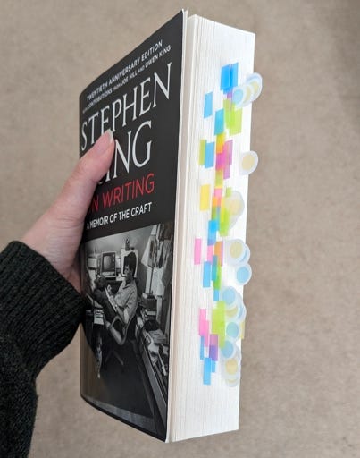 Katheryn's hand holds the book On Writing by Stephen King so that the edge of the pages are visible. Brightly coloured tabs stick out from the page block where she marked things of note.