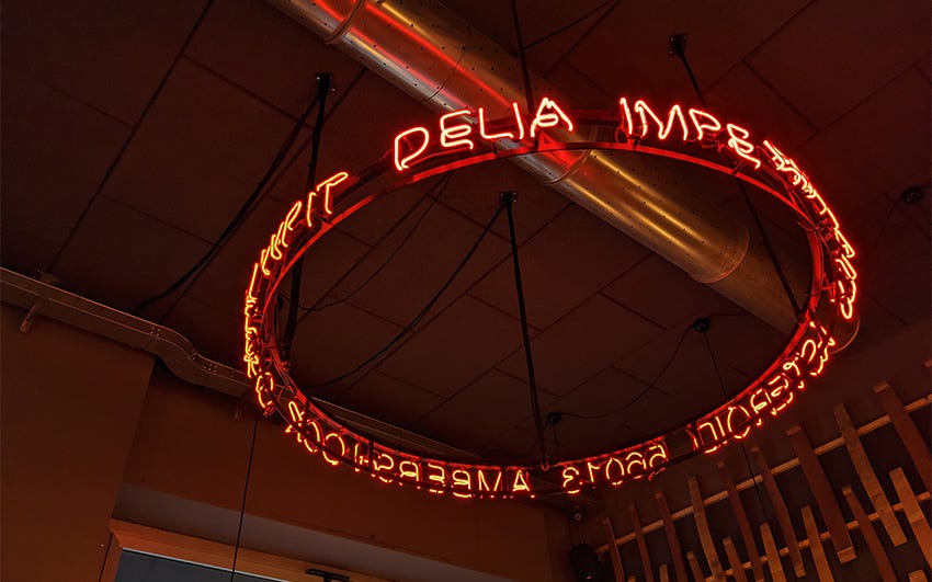A circular red neon lamp dangling from the ceiling of a Milan craft beer bar.