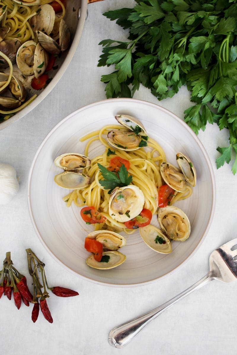 overhead image of linguine con le vongole on a white plate and parsley in background. 