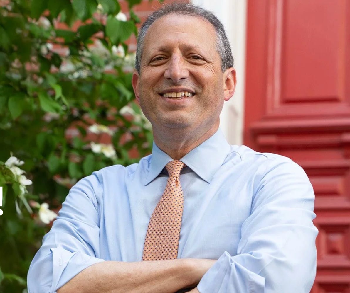 New York City Comptroller Brad Lander standing with his arms crossed. He's smiling with short graying hair. he's wearing a blue shirt and a orange polka dot tie. he's standing in front of a tree and a red background New York City Comptroller Brad Lander standing with his arms crossed. He's smiling with short graying hair. he's wearing a blue shirt and a orange polka dot tie. he's standing in front of a tree and a red background