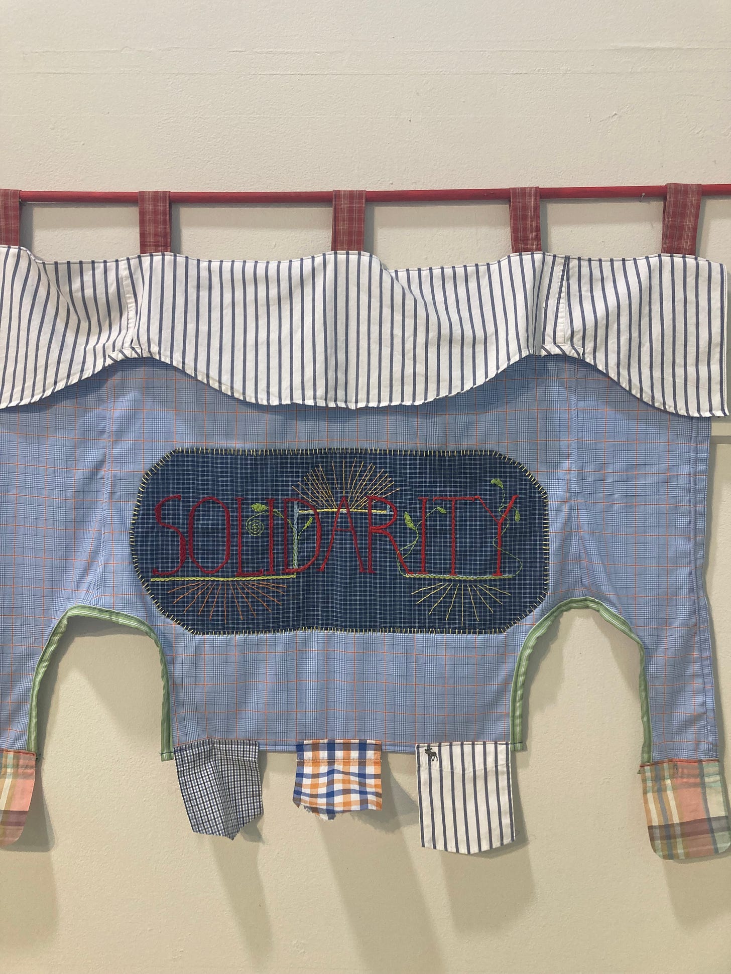 an embroidered, quilted flag with blue, white, red, and yellow patterns and the word "SOLIDARITY" stitched into it with stitches of leaves