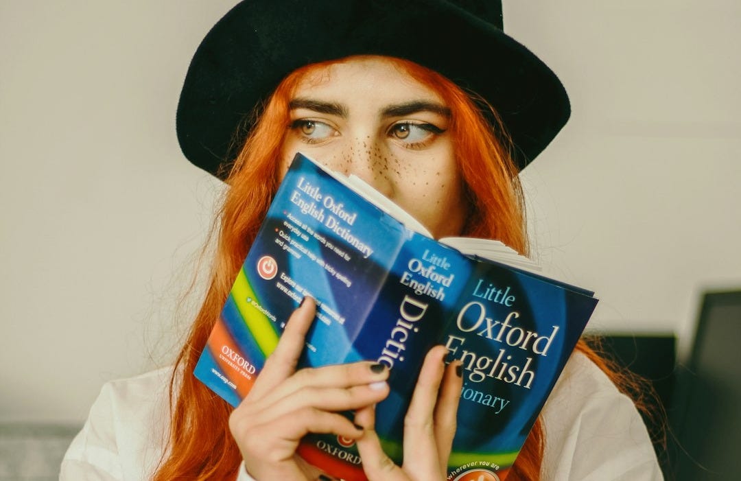 A woman with red hair is holding a dictionary.