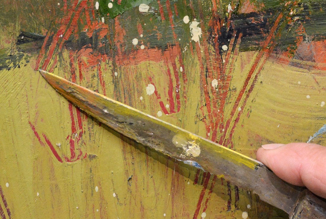 A hand holding a knife over a painting

Description automatically generated