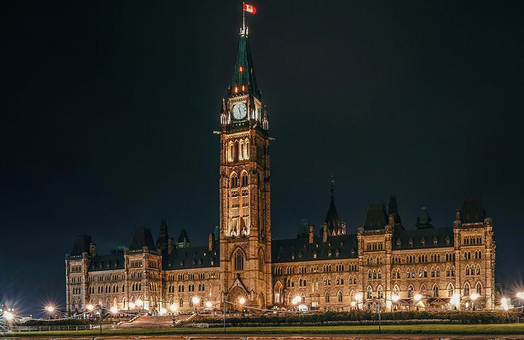 Illuminated Gothic building at night with a central clock tower. Reflective water in foreground. Romantic and serene atmosphere. Illuminated Gothic building at night with a central clock tower. Reflective water in foreground. Romantic and serene atmosphere.