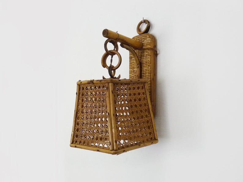 May include: A woven wicker wall sconce with a square lampshade. The sconce is made of natural bamboo and has a simple, rustic design. May include: A woven wicker wall sconce with a square lampshade. The sconce is made of natural bamboo and has a simple, rustic design.