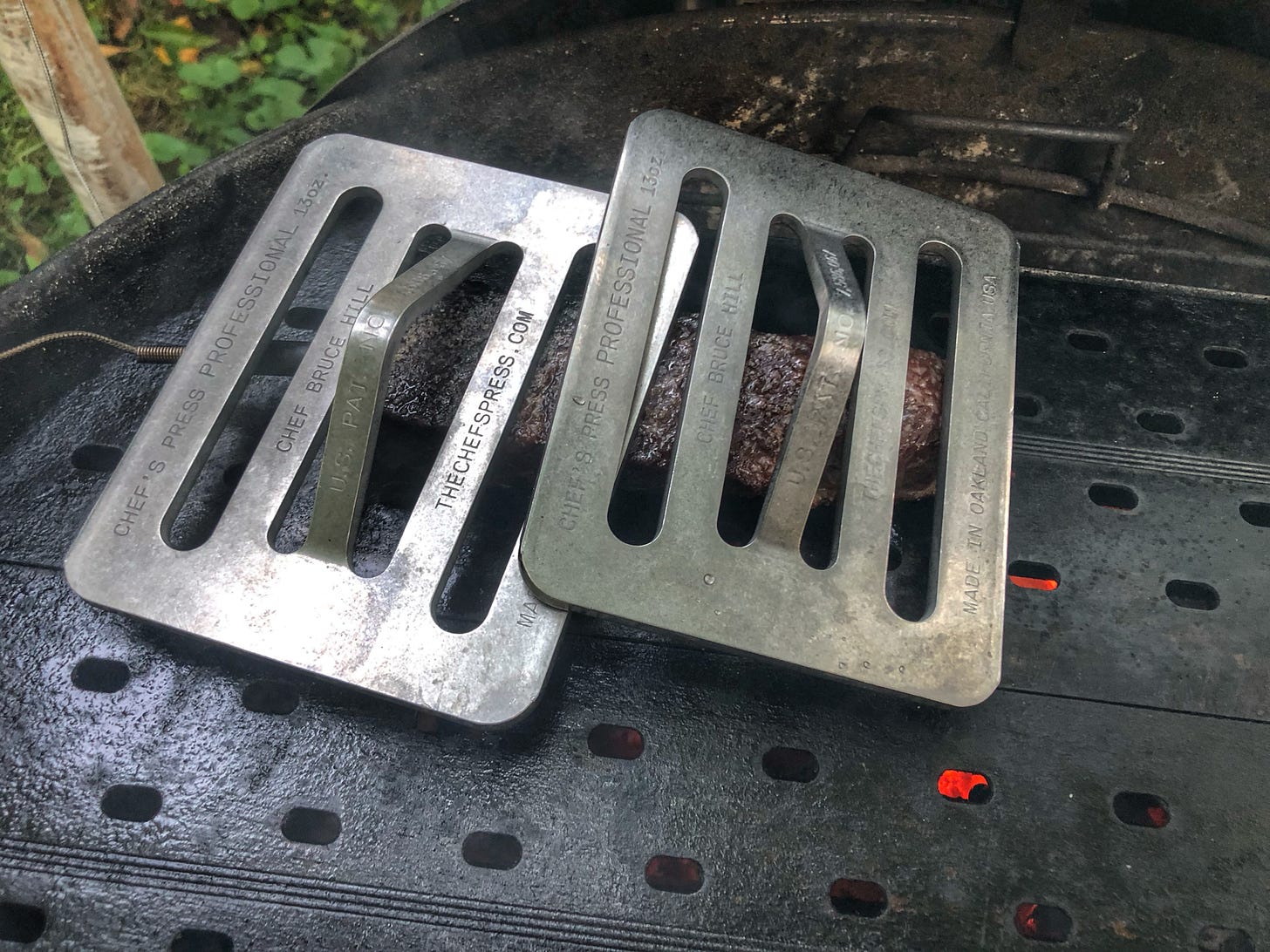 Two Chef's Presses weighing down a steak on a charcoal grill covered with GrillGrates