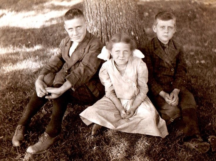 This may contain: an old black and white photo of three children sitting under a tree This may contain: an old black and white photo of three children sitting under a tree
