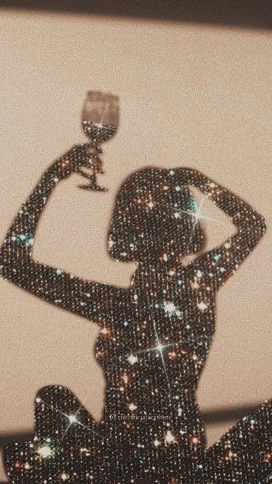 This may contain: a woman holding a wine glass in front of her face with glitters on it